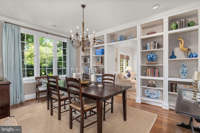 dining space featuring hardwood / wood-style flooring, ornamental molding, built in shelves, and a chandelier