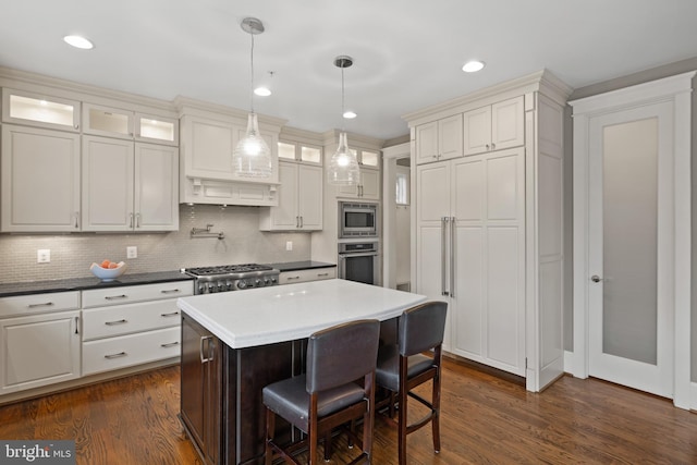 kitchen with dark wood-type flooring, a breakfast bar, decorative light fixtures, a center island, and appliances with stainless steel finishes