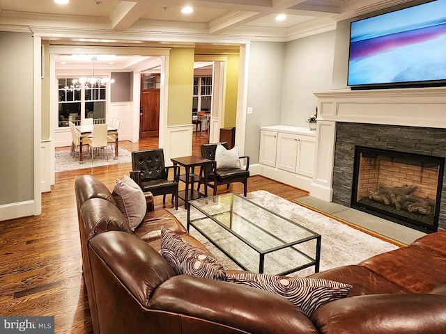 living room featuring a stone fireplace, beamed ceiling, ornamental molding, light hardwood / wood-style floors, and an inviting chandelier