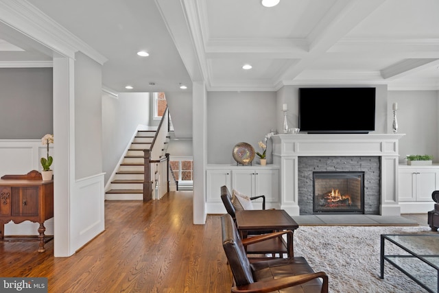 living room with wood-type flooring, a fireplace, ornamental molding, and beamed ceiling