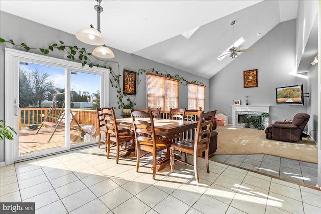 dining space with high vaulted ceiling, a skylight, light tile patterned floors, ceiling fan, and a high end fireplace