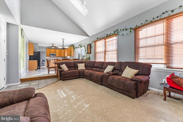 living room with light carpet, a skylight, light tile patterned floors, baseboards, and high vaulted ceiling