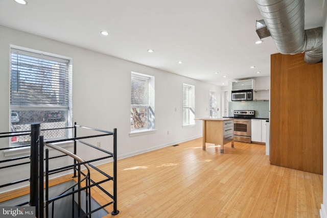 kitchen featuring light wood-type flooring, a healthy amount of sunlight, stainless steel appliances, and backsplash