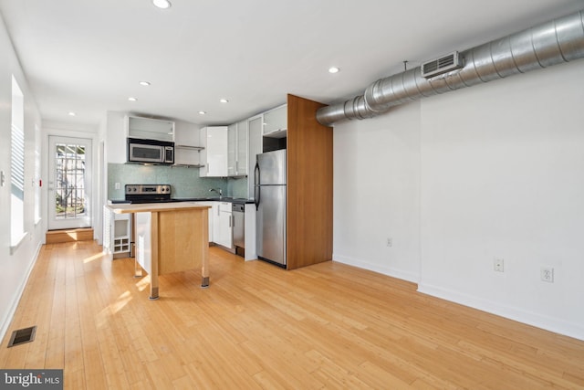 kitchen featuring appliances with stainless steel finishes, visible vents, decorative backsplash, and light wood finished floors