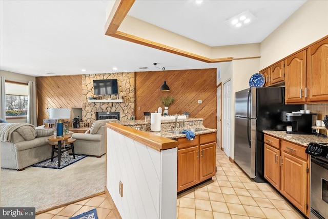 kitchen featuring light tile patterned floors, sink, stove, a fireplace, and wood walls