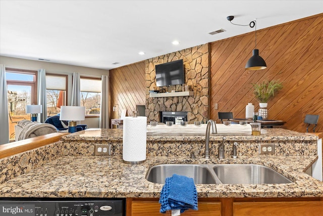 kitchen with sink, hanging light fixtures, wooden walls, light stone countertops, and a stone fireplace