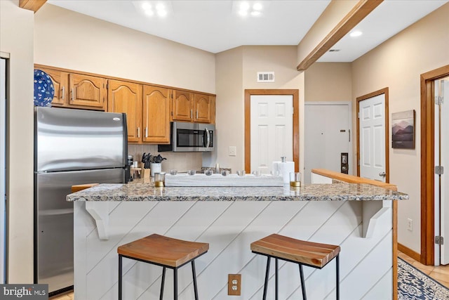 kitchen with light stone countertops, stainless steel appliances, and a kitchen breakfast bar