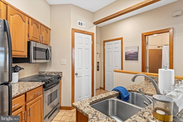 kitchen with sink, appliances with stainless steel finishes, backsplash, light stone counters, and light tile patterned flooring