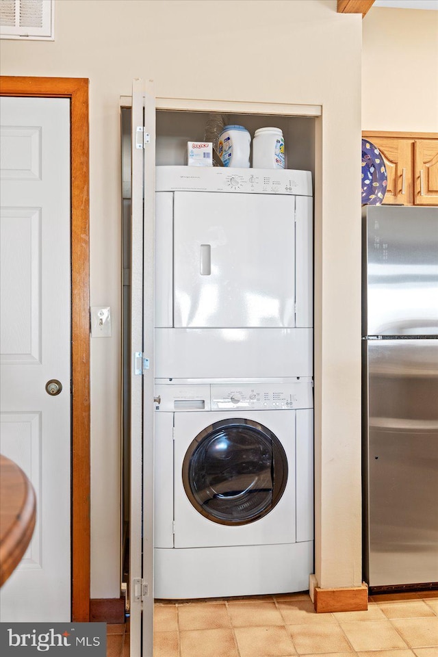 laundry area with stacked washer / drying machine and light tile patterned floors