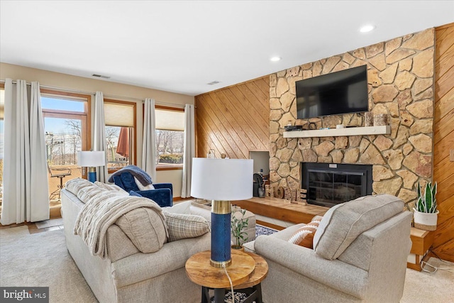 living room with light colored carpet, a stone fireplace, and wood walls