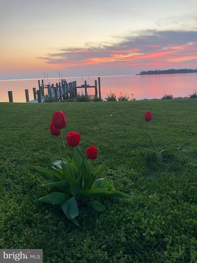 yard at dusk with a dock, a water view, and boat lift