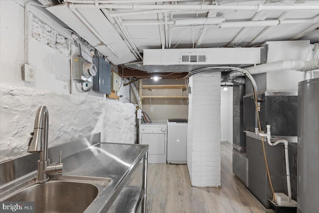 basement featuring sink, light wood-type flooring, electric panel, independent washer and dryer, and water heater