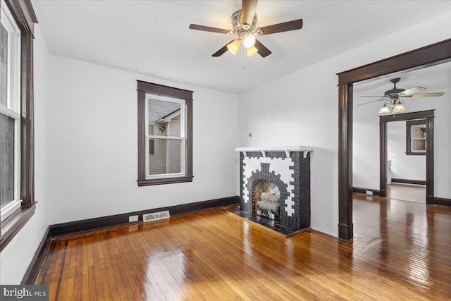 unfurnished living room with ceiling fan, hardwood / wood-style floors, and a brick fireplace