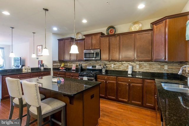 kitchen with sink, appliances with stainless steel finishes, hanging light fixtures, hardwood / wood-style floors, and dark stone counters