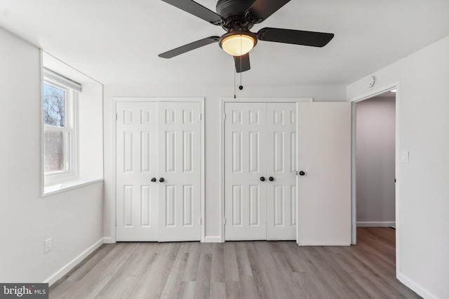 unfurnished bedroom with baseboards, wood finished floors, a ceiling fan, and multiple closets