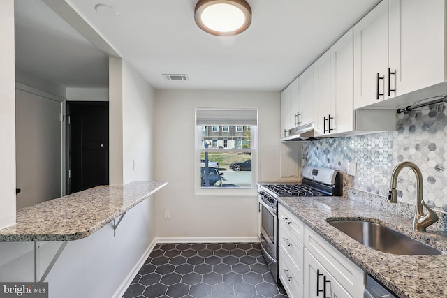 kitchen with decorative backsplash, white cabinets, stainless steel gas stove, a sink, and under cabinet range hood