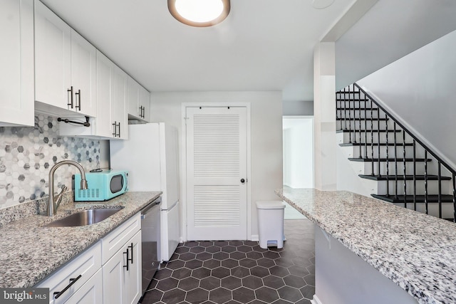 kitchen featuring light stone counters, a sink, white cabinets, stainless steel dishwasher, and tasteful backsplash
