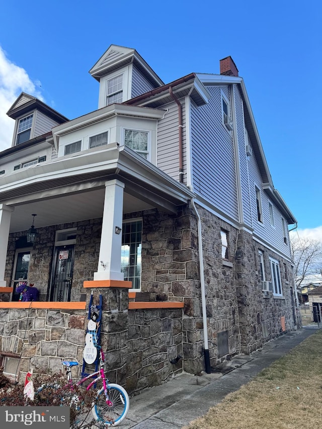 view of side of home with stone siding, a porch, a chimney, and cooling unit