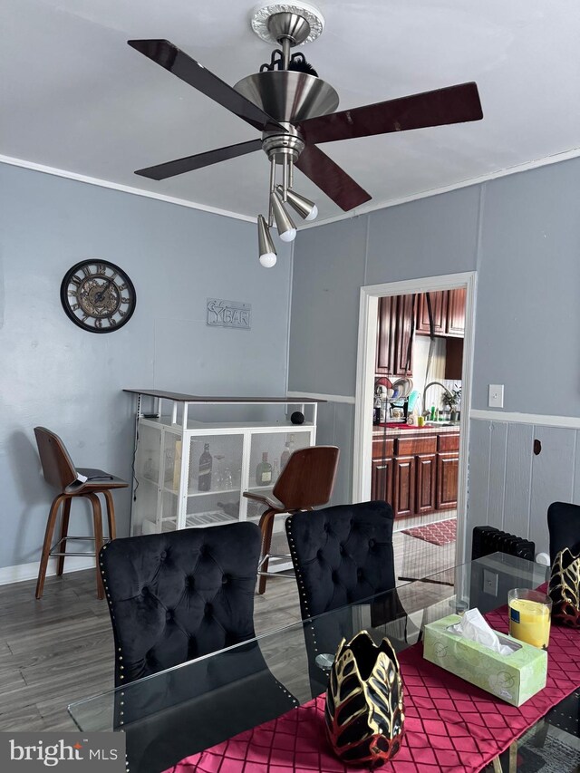 interior space with crown molding, a wainscoted wall, ceiling fan, and wood finished floors