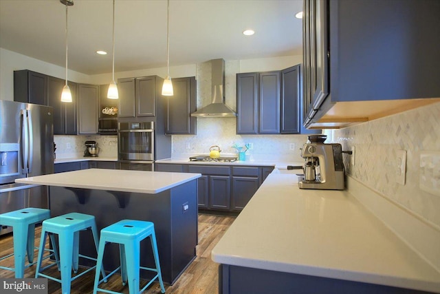 kitchen with a kitchen bar, decorative backsplash, a center island, stainless steel appliances, and wall chimney exhaust hood