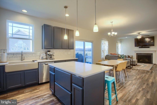 kitchen with sink, hanging light fixtures, wood-type flooring, a kitchen island, and stainless steel dishwasher