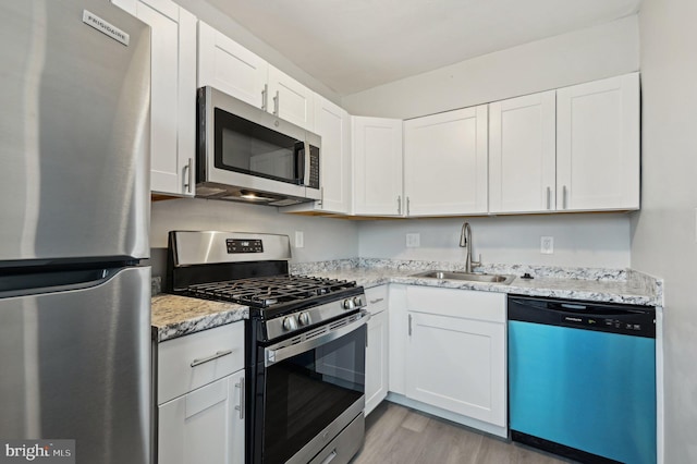 kitchen with stainless steel appliances, sink, white cabinets, and light stone counters