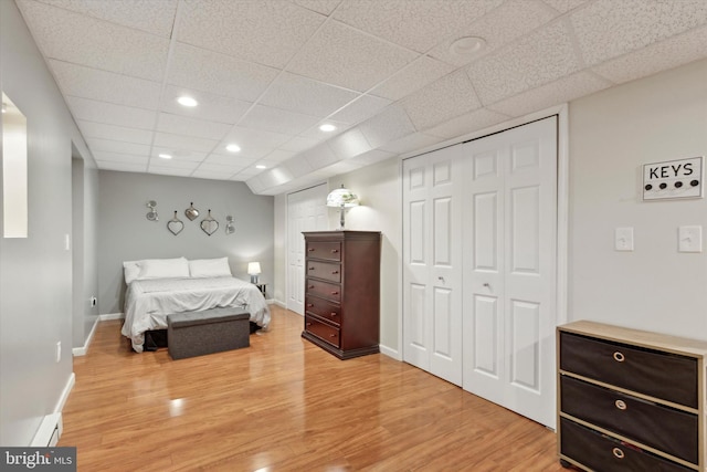 bedroom with baseboard heating, a drop ceiling, a closet, and light wood-type flooring