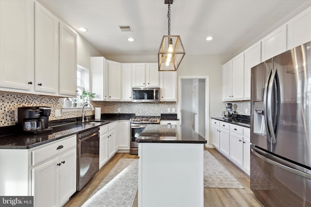 kitchen featuring sink, appliances with stainless steel finishes, a center island, white cabinets, and decorative light fixtures