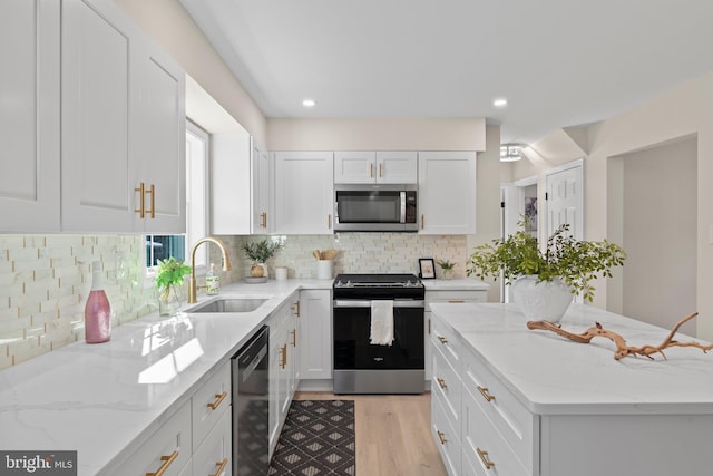 kitchen featuring light hardwood / wood-style flooring, appliances with stainless steel finishes, light stone counters, white cabinets, and decorative backsplash