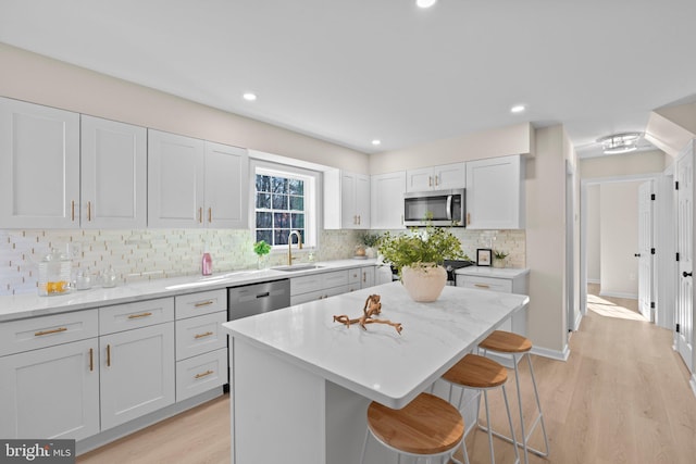 kitchen with sink, a center island, appliances with stainless steel finishes, a kitchen breakfast bar, and light stone countertops