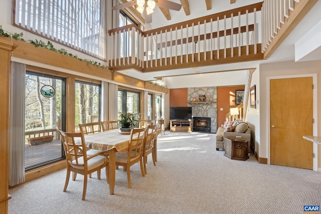 carpeted dining space with ceiling fan, a towering ceiling, and a stone fireplace