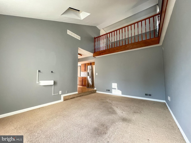 unfurnished living room with carpet, high vaulted ceiling, and a skylight