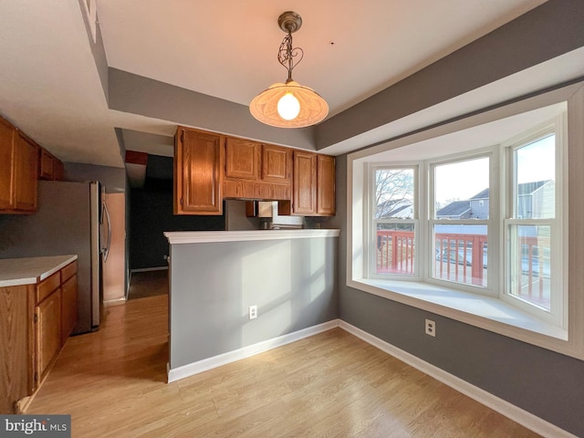 kitchen with light hardwood / wood-style flooring, kitchen peninsula, stainless steel fridge, and decorative light fixtures