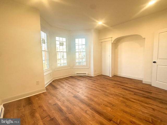 empty room featuring a baseboard heating unit and dark wood-type flooring