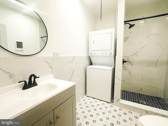 bathroom with tiled shower, toilet, tile walls, vanity, and stacked washing maching and dryer