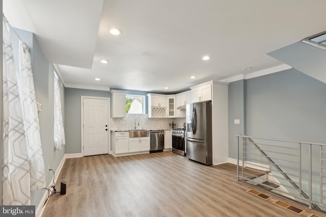 kitchen with tasteful backsplash, ornamental molding, appliances with stainless steel finishes, and white cabinets