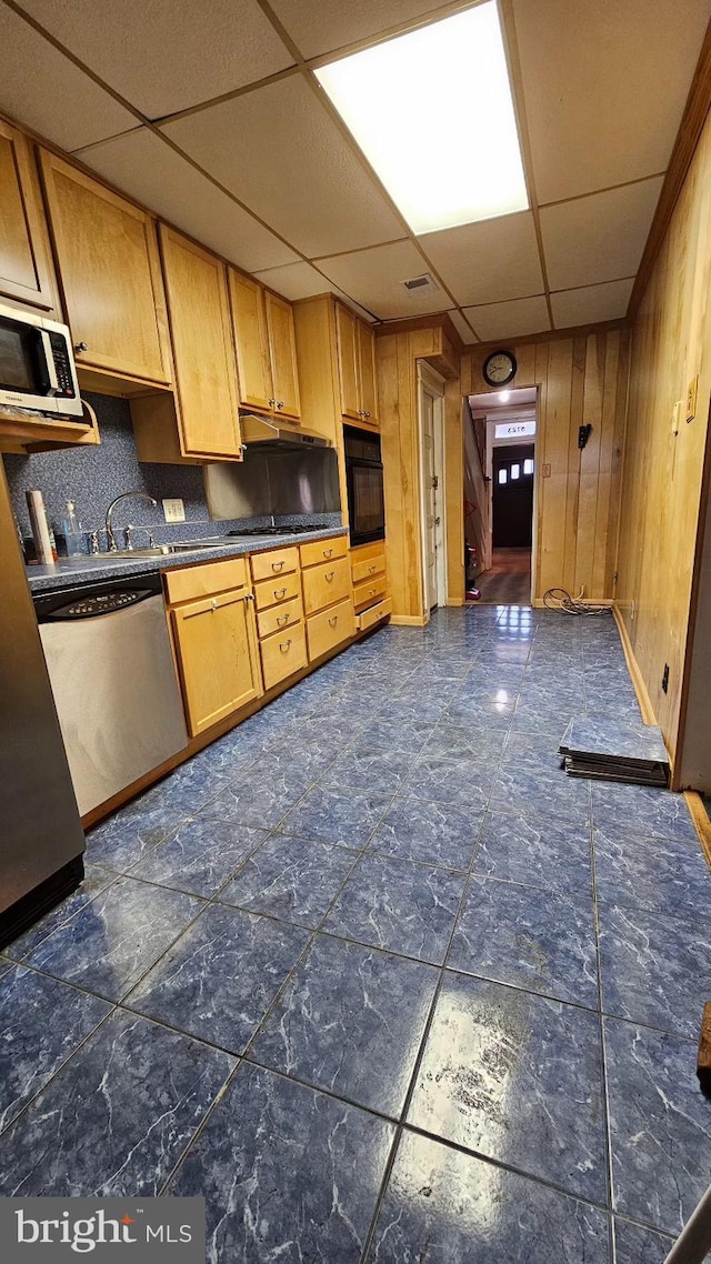 kitchen with appliances with stainless steel finishes, a paneled ceiling, backsplash, and wood walls