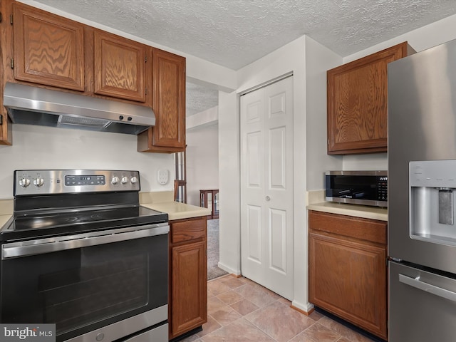 kitchen featuring a textured ceiling, light countertops, appliances with stainless steel finishes, wall chimney exhaust hood, and brown cabinetry