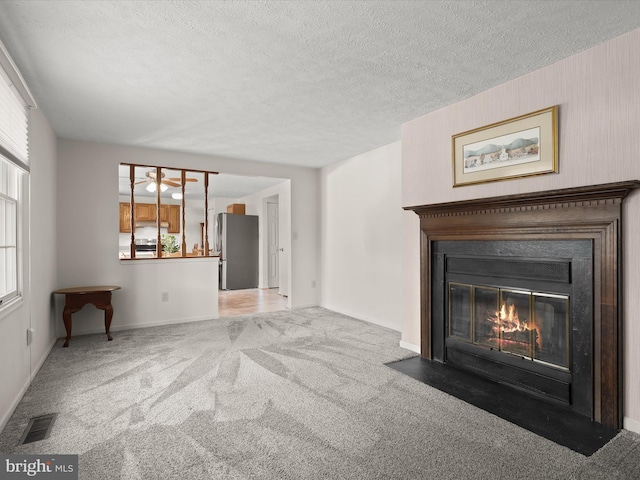 unfurnished living room with carpet, visible vents, a fireplace with flush hearth, a textured ceiling, and baseboards