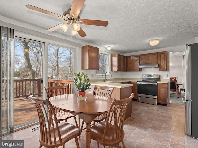 kitchen featuring brown cabinetry, appliances with stainless steel finishes, light countertops, under cabinet range hood, and a sink