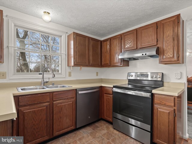 kitchen with light countertops, appliances with stainless steel finishes, a sink, a textured ceiling, and under cabinet range hood