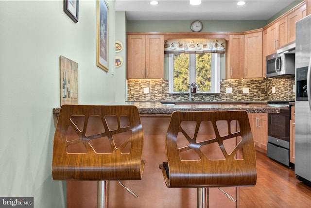 kitchen with appliances with stainless steel finishes, a breakfast bar, light hardwood / wood-style floors, and decorative backsplash