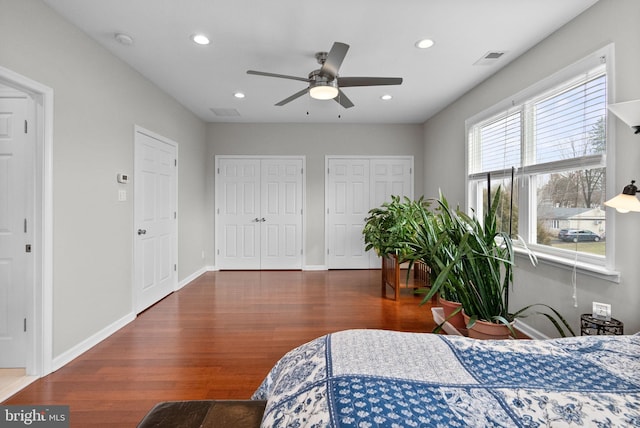 bedroom featuring multiple closets, ceiling fan, and dark hardwood / wood-style flooring