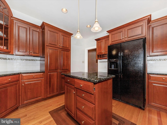 kitchen with black fridge, decorative light fixtures, dark stone countertops, light hardwood / wood-style floors, and decorative backsplash