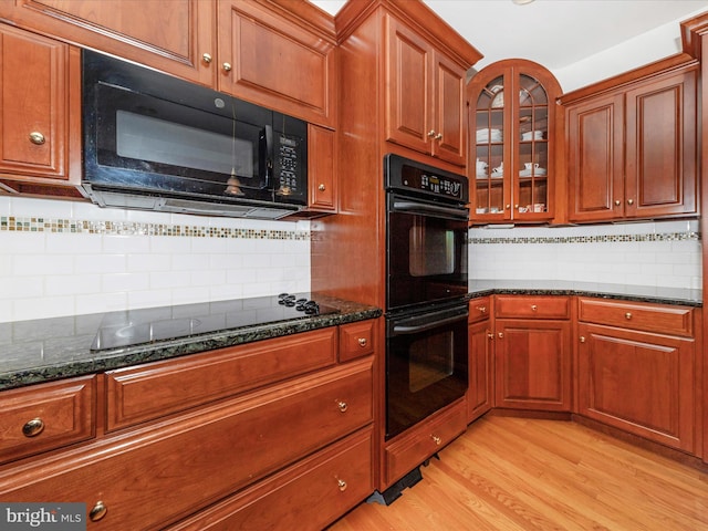 kitchen with tasteful backsplash, dark stone countertops, light hardwood / wood-style floors, and black appliances