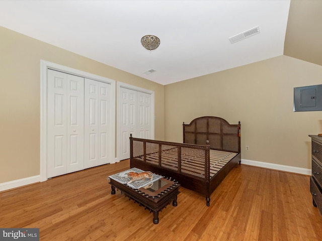 bedroom featuring vaulted ceiling, electric panel, light wood-type flooring, and two closets