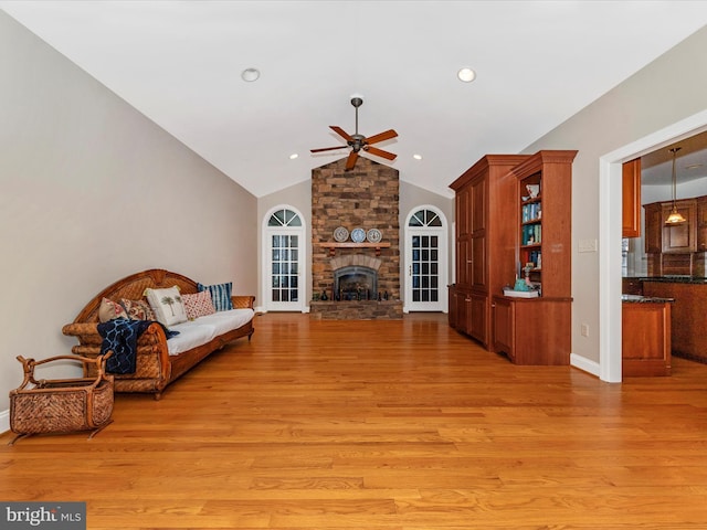 living room featuring high vaulted ceiling, a stone fireplace, light hardwood / wood-style floors, and ceiling fan