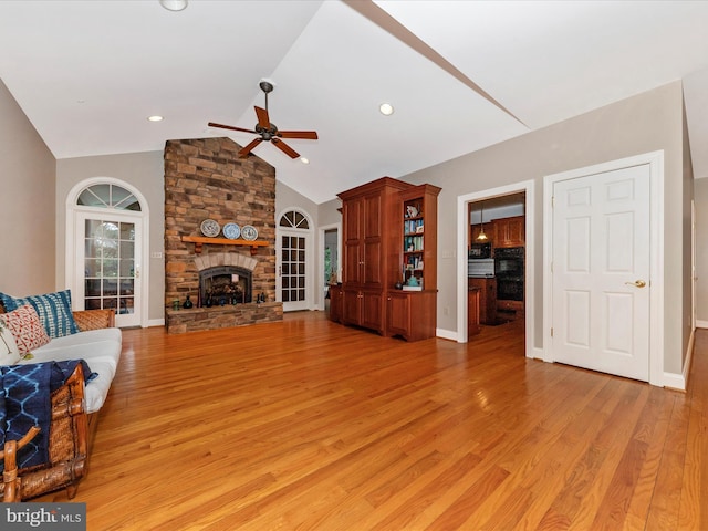 living room featuring ceiling fan, lofted ceiling, a stone fireplace, and light wood-type flooring