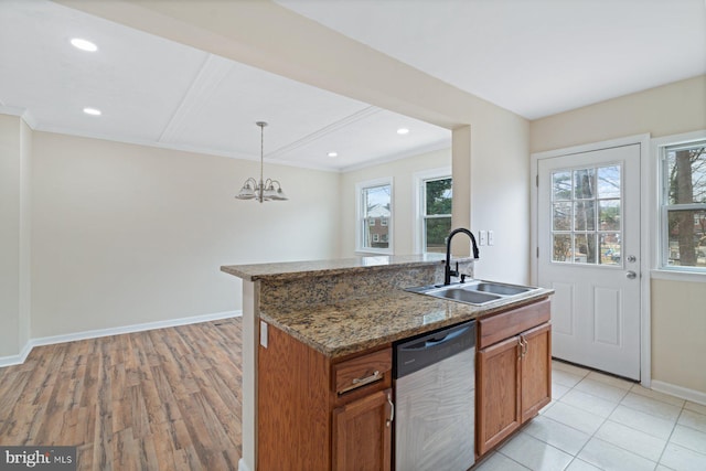 kitchen featuring stainless steel dishwasher, an island with sink, decorative light fixtures, and sink