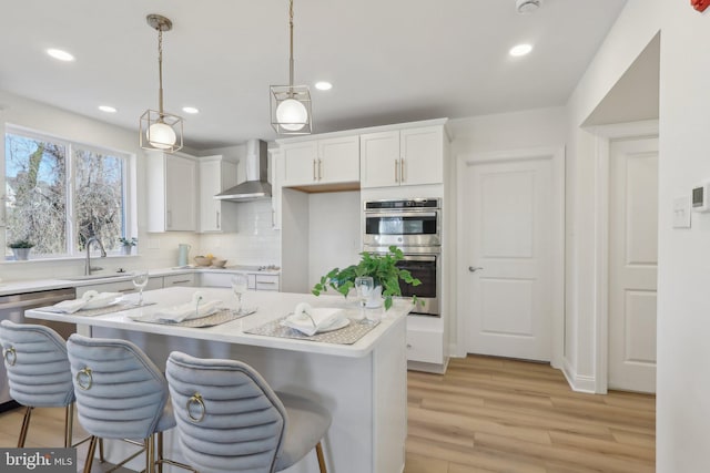 kitchen featuring sink, double oven, white cabinets, decorative light fixtures, and wall chimney exhaust hood